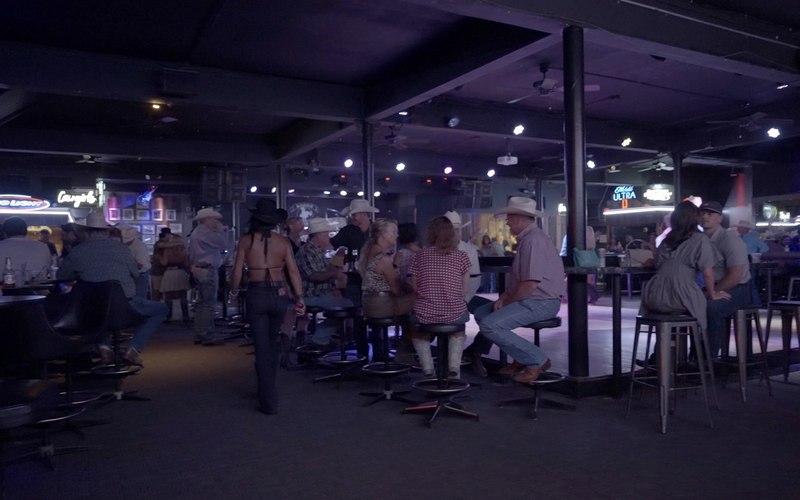 A wide view down the length of the hall, high-tops and the bar with a full room