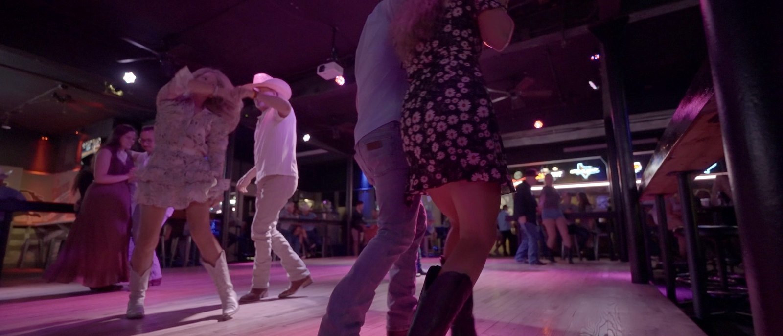Couples dancing under a pink wash on the Rodeo Exchange dance floor
