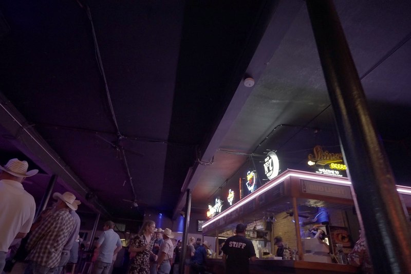 People walking the covered boardwalk past neon signs in the Stockyards